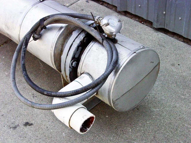 One end of heat exchanger showing end cap/head, gray liquid-tight flex conduit with wiring, PVC elbow outlet below, and small instrument fitting on top — surface rust and wear