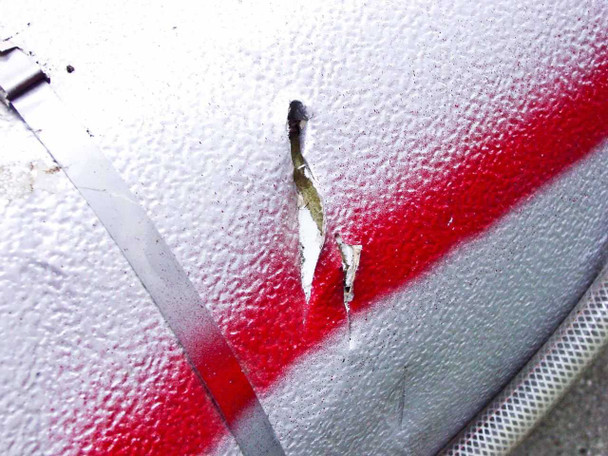 Close-up of outer insulation jacket on shell showing a tear/cut in the metal cladding with yellow insulation material exposed beneath, red spray-paint stripe visible