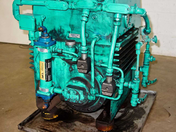 Kinney KTC112 rear view — drive belt/coupling end, oil lines, piping fittings, and skid base with oil accumulation visible