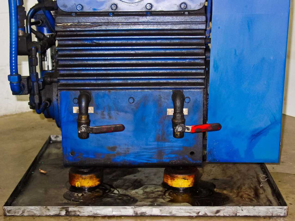 Tuthill KTC112 rear base view showing two manual drain valves, oil pooling visible on drip pan beneath anti-vibration mounts
