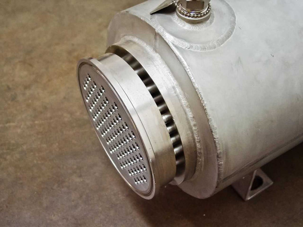 Angled close-up of tube sheet face — rows of tube holes, serrated-face flange, and top nozzle fitting visible