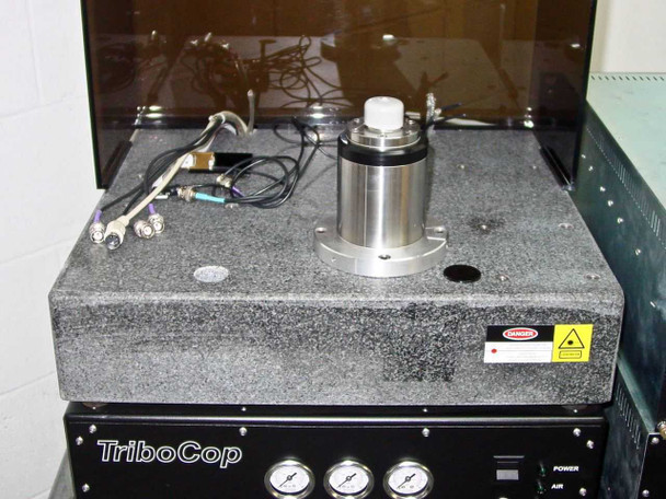 TTI T9000 TriboCop Spinstand top view — granite surface plate with spindle motor/head assembly mounted centrally, BNC and signal cables, laser warning label, with TriboCop base unit visible below