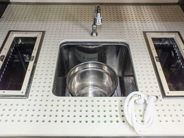 Top-down view of center sink area with stainless steel bowl insert, faucet, and two flanking ultrasonic bath tanks on perforated surface