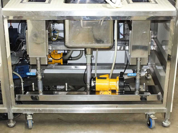 Under-bench view from front showing plumbing, hoses, two yellow Pan World magnet pumps, and electrical wiring beneath stainless steel frame on casters