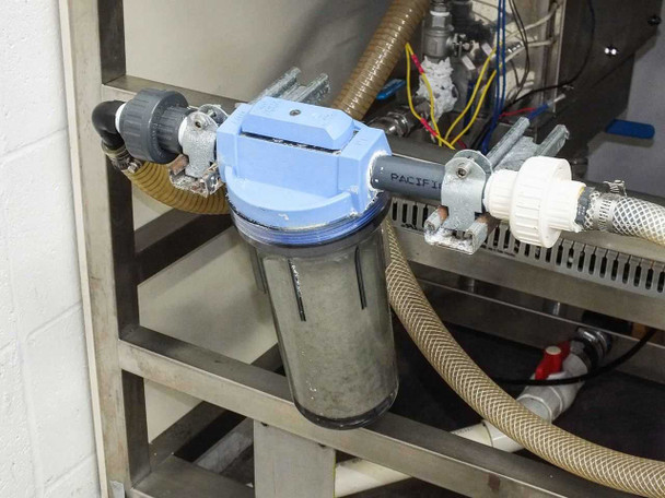 Close-up of blue Pacific inline water filter housing with clear sediment bowl — mounted in rear plumbing circuit under bench