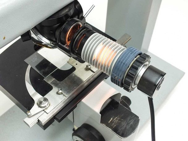 Carl Zeiss microscope illuminator light source close-up — lamp housing lit and glowing, bellows accordion focus tube, filter ring, confirming bulb is functional
