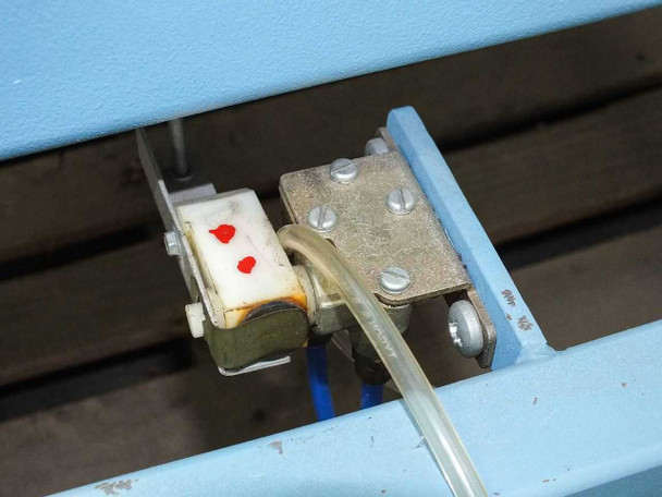Close-up of pneumatic solenoid valve with red indicator dots and clear tubing attached to blue frame