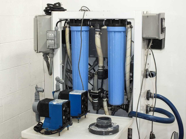 Rear view of USFilter system showing three large blue filter housings, dual Pulsatron pumps, and associated plumbing and hoses