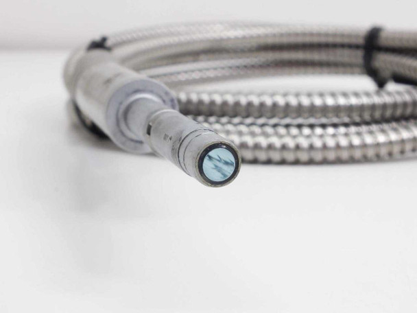 Lumatec fiber optic microscope light guide close-up of source-end barrel connector with blue fiber bundle face visible, stainless armored cable coiled in background