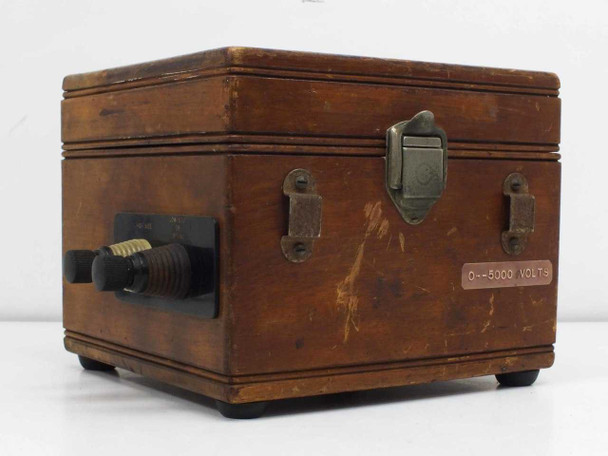 Rear/side view of wooden case closed, showing brass latch hardware, corner wear, and red label reading 0–5000 VOLTS