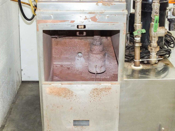 Interior view of stainless steel collection basin showing heavy mineral scale buildup and float valve assembly