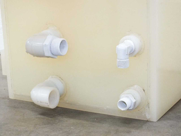 Bottom-corner view of PTFE wafer etch bath showing four PVC inlet/outlet fittings with elbow and straight connectors