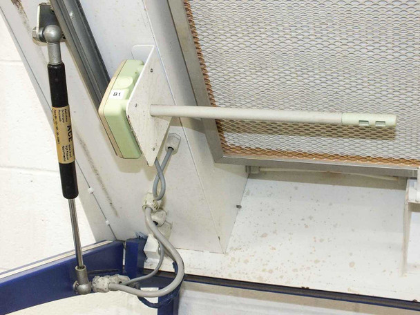 Close-up of gas strut hinge mechanism and ionizer probe bracket on interior left side wall, with mesh HEPA filter face and wiring visible