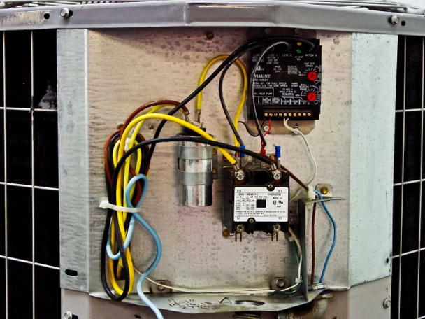 Outdoor condenser electrical compartment — Totaline P251-0083H fan speed/motor protection board, run capacitor, and contactor with multi-color wiring harness visible