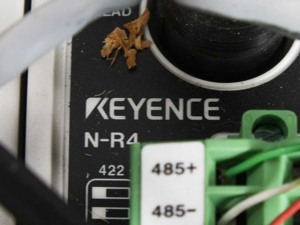 Close-up of Keyence N-R4 communication amplifier label showing model number, RS-422 and RS-485 terminal connections with debris visible on surface