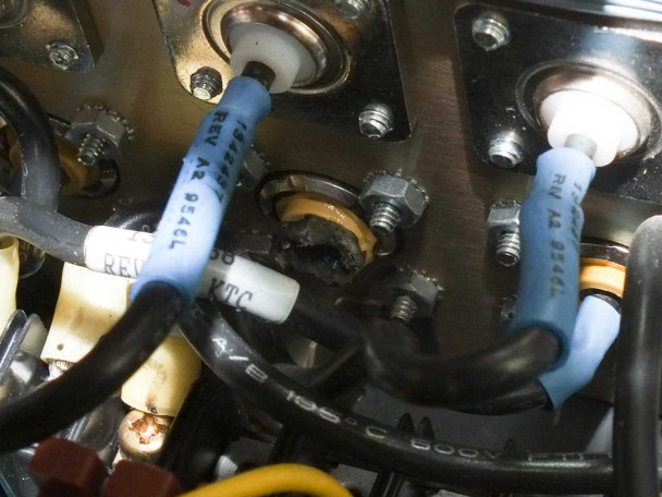 Advanced Energy PE-10/20K interior view showing burned damage at RF connector area with charred residue and blue wire leads labeled REV A2, partially disassembled chassis