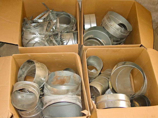 Four open cardboard boxes containing assorted galvanized sheet metal duct fittings including collars, couplings, reducers, and perforated metal strapping