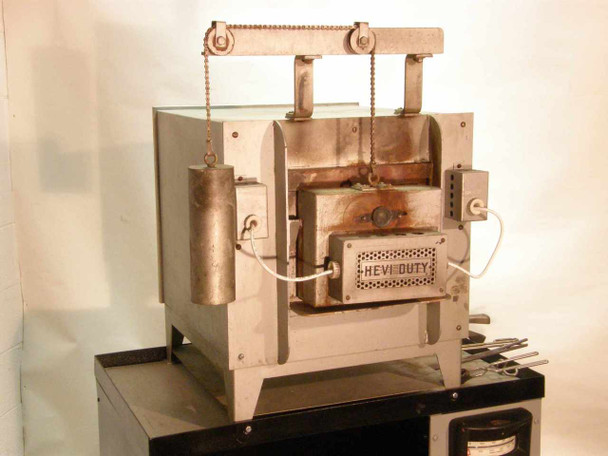 Hevi-Duty HDT-5610 box furnace three-quarter front view — counterweight door lift mechanism and chain visible, HEVI DUTY nameplate on door, refractory brick surround showing heat discoloration