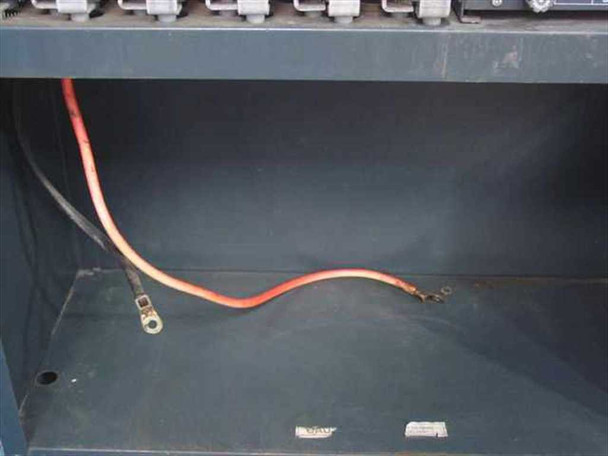 UPS cabinet lower battery compartment showing red and black heavy-gauge battery cables with ring terminals on empty shelf