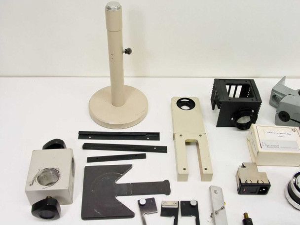 Close-up of microscope stand post with base, black filter cube housing, ivory bracket assembly, and optical head components laid out on table