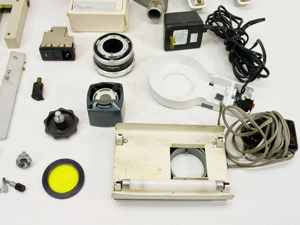 Close view of power switch module, chrome lens ring, gray cube module, knobs, yellow filter disc, white ring light, and slide stage platform with apertures