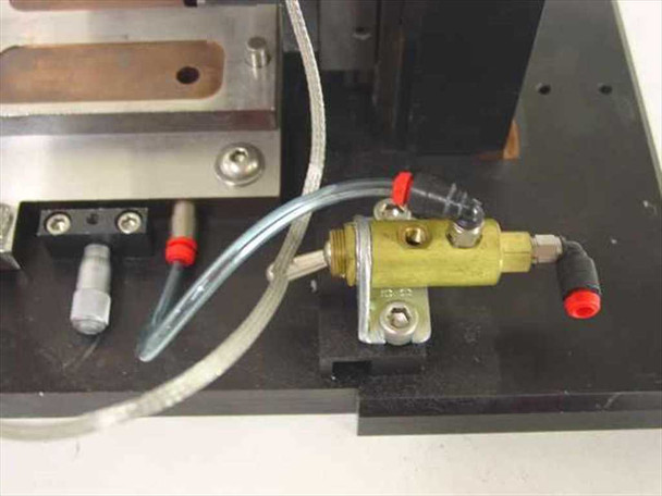 Close-up of brass pneumatic valve manifold with red-capped push-fit fittings, clear pneumatic tubing, and two cylindrical contact probes on black base