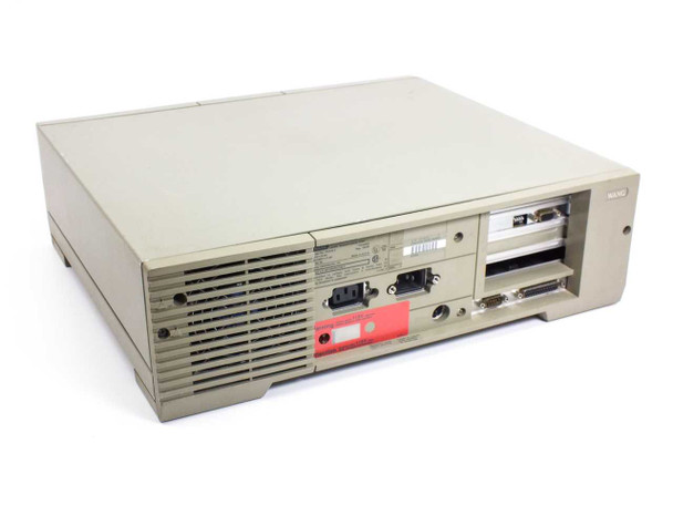 Wang PC240-3 desktop computer — rear three-quarter view showing IEC power inlet, ventilation grille, DB9 serial port, DB25 parallel port, and red voltage warning label