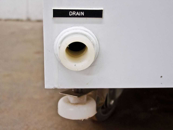 Cabinet base drain port labeled DRAIN with white PVC fitting and caster wheel visible below