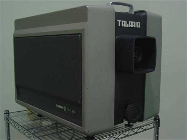GE Talaria PJ5055C1 light valve projector — right front three-quarter view showing General Electric badge and Talaria name on dark lens housing, unit on wire shelf