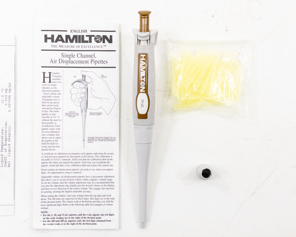 Hamilton 55019-07 single-channel fixed volume pipette showing gold-accented SoftGrip body with 50µL volume marking, alongside calibration certificate, manual, tips, and calibration tool