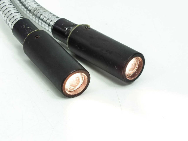Dual output tips illuminated, showing bright copper-colored fiber bundle faces lit from within both 19mm cylindrical output housings