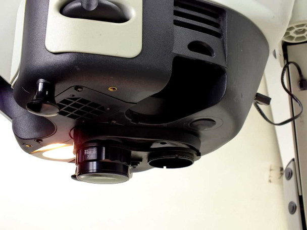 Bottom-up view from alternate angle showing one amber-lit bulb, installed X4 objective, empty opposite bay, and power cable routed along arm