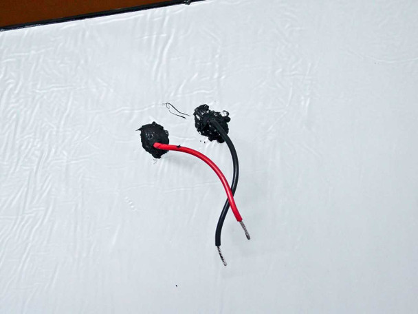 Underside of Uni-Solar PVL-136 showing bottom-facing 4-inch red and black DC output wires with weatherproof quick-connect terminals on white adhesive backing