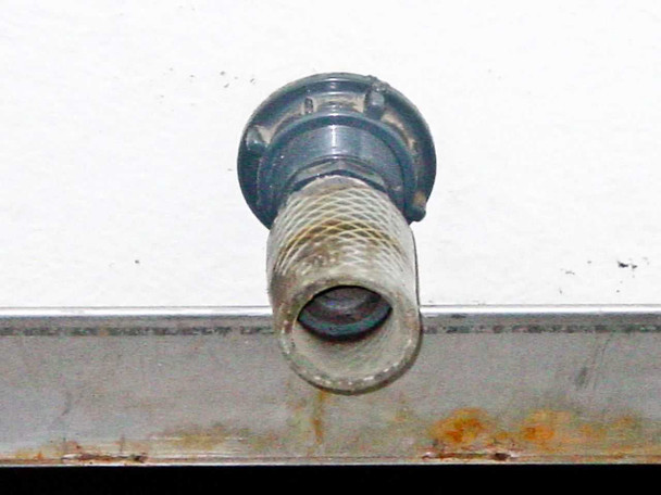 Poly tank side outlet fitting close-up — threaded hose-barb style fitting with chemical residue and rust staining on metal frame below