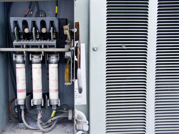 Trane CGAF-C20 electrical section — three-pole fused disconnect with large cylindrical fuses and disconnect handle, adjacent louvered condenser panel