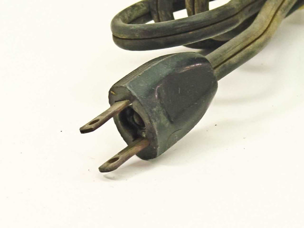 Closeup of vintage two-prong power plug attached to original cloth-covered power cord, showing aged rubber and brass prongs