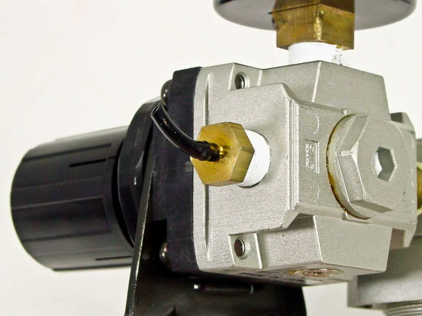 Close-up of SMC NAR2000 regulator body — brass pressure port with wire lead, black adjustment knob, and top brass fitting visible