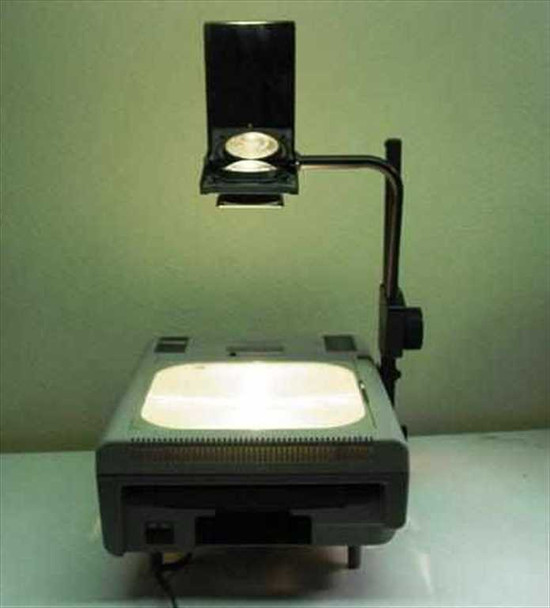 Dukane 663 portable overhead projector shown fully deployed with projection head raised on arm and stage lamp lit — front view on table