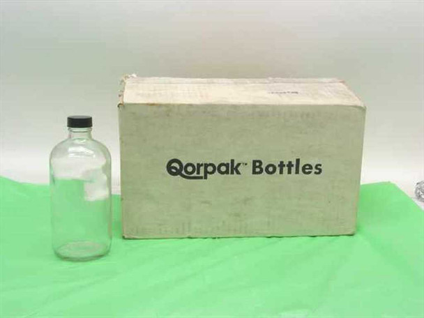 Qorpak 16 oz clear glass Boston Round bottle with black cap shown next to original Qorpak Bottles shipping box