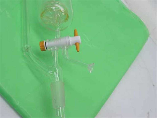 Detail of glass stopcock assembly with white PTFE body and orange caps, plus curved glass side-arm and small round-bottom flask connection