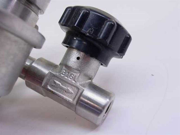 Close-up of 316L stainless steel needle valve body with black adjustment knob and directional flow arrow stamped on body