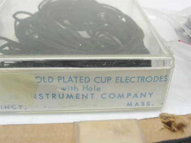 Clear plastic storage box close-up showing label: Gold Plated Cup Electrodes with Hole, Instrument Company, Quincy Massachusetts