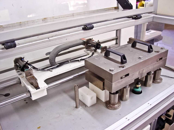 Close-up of boat shuttle tooling fixture on linear rails – showing handle-equipped metal platen, guide posts, and pneumatic actuator assembly
