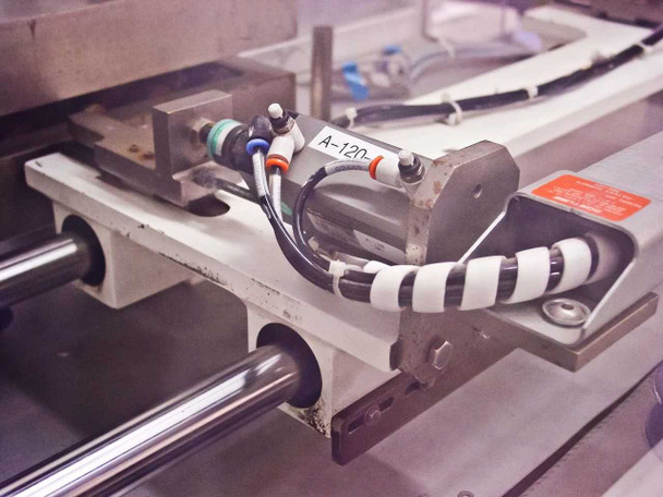 Shuttle carriage close-up – showing label marked A-120, pneumatic fittings with push-to-connect tubing, sensor, and linear rail mounting