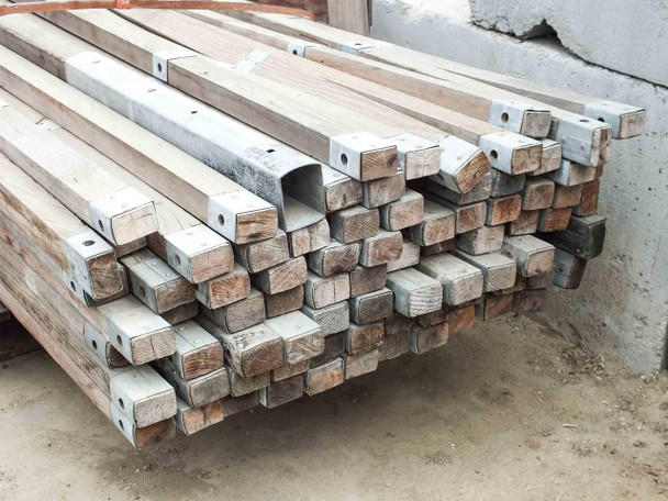 End-on view of stacked Tucker Mfg military ridge poles showing weathered wood bodies and galvanized steel end cap fittings with bolt holes