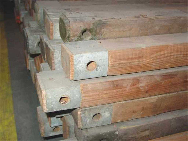 End view of military wood ridge beam tent poles showing steel reinforcement end caps with bolt holes stacked on pallet