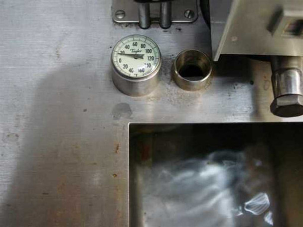 Haake F 4391 tank lid top view — Taylor dial thermometer mounted on lid surface, threaded port opening, rust spots and surface staining visible on stainless lid, tank interior partially visible