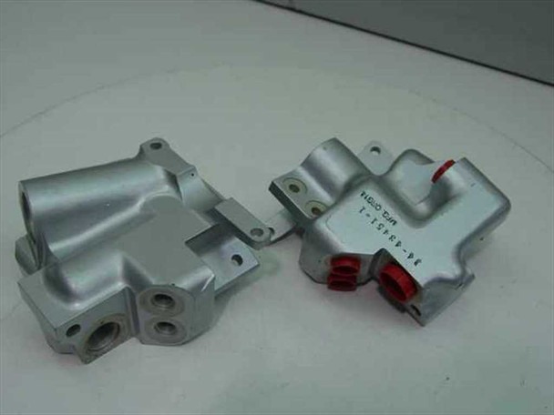 Two silver aluminum valve bodies part 14-43451-1 side by side — one with red plastic port covers, one without