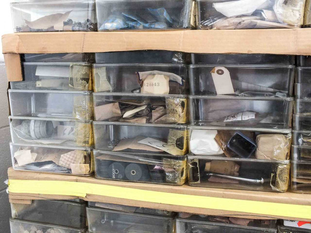Close-up of several organizer drawers showing small machined parts, lens components, and tagged film camera hardware