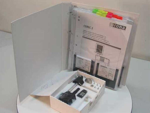 Sirona CEREC 2 manual open showing tabbed dividers and two EUROPA-branded CEREC 2 software floppy diskettes, with open maintenance kit box containing tools and small components